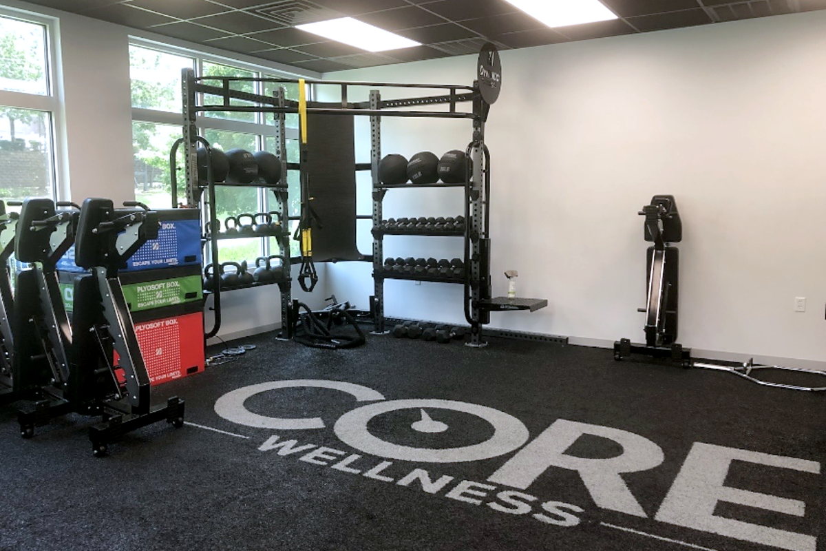 The Core Wellness training floor with a squat rack, kettlebells, dumbbells, medicine balls, plyometric boxes, and a rower.